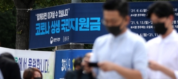 코로나 상생 국민지원금 신청이 시작된 지난 6일 오전 서울 중로구 도심에서 시민들이 '코로나 상생 국민지원금' 신청 안내 현수막 앞을 지나고 있다. 2021.09.06.