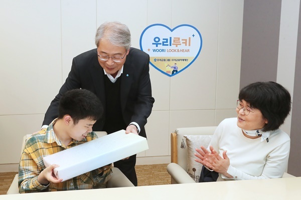 우리금융그룹 우리금융미래재단은 지난 2일 서울 중구에 있는 우리금융 본사에서 「우리 루키(Look & Hear) 프로젝트」를 통해 시·청각 수술비를 지원받은 수혜자와 가족 12명을 초청해 새해맞이 행사를 가졌다. 임종룡 우리금융그룹 임종룡 회장(가운데)이 초청 가족에게 선물을 전달하고 있다. ⓒ 파이낸셜데일리 / 우리금융